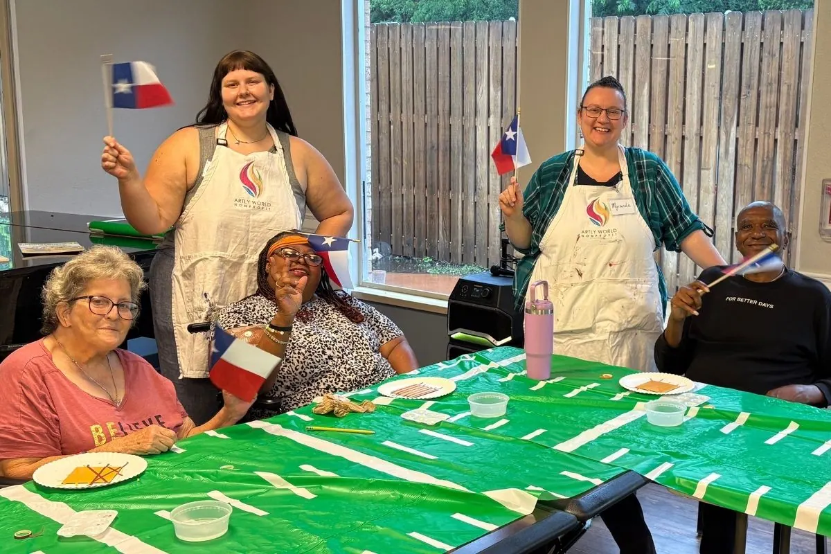 Two teaching artists and three residents wave Texas flags at a craft table.