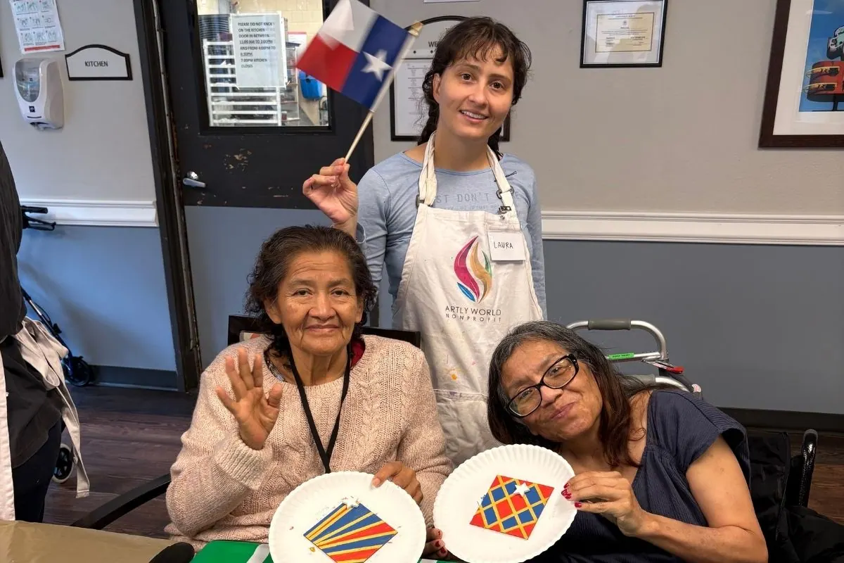 A teaching artist waves a Texas flag behind two residents holding paper plate kite paintings.