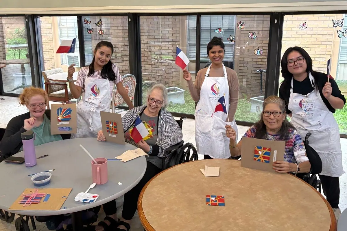 Three teaching artists and three residents display star shaped paintings while waving small paper flags.