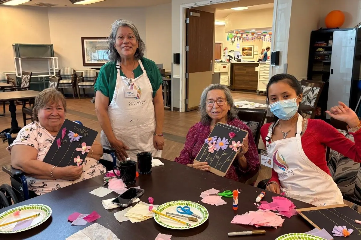 Two teaching artists and two residents hold paper artwork decorated with tissue paper flowers.