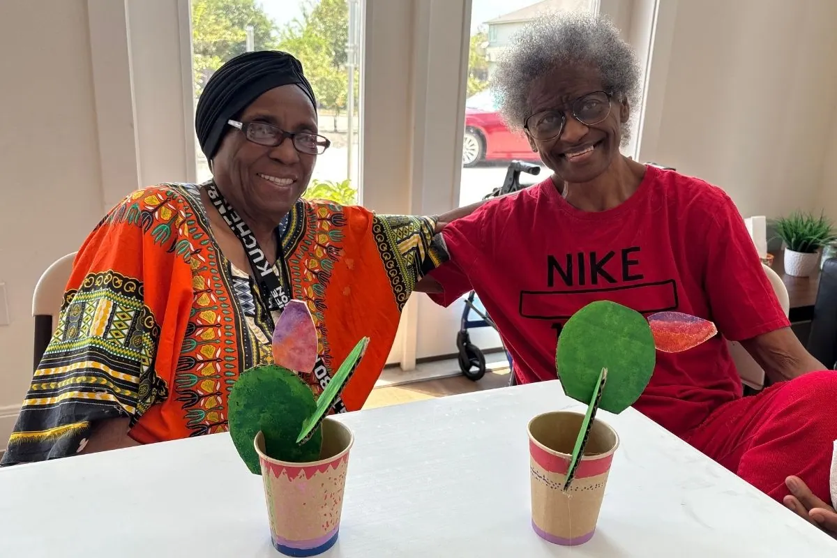 Two residents sit together, each holding a paper cup planted with a painted cactus.