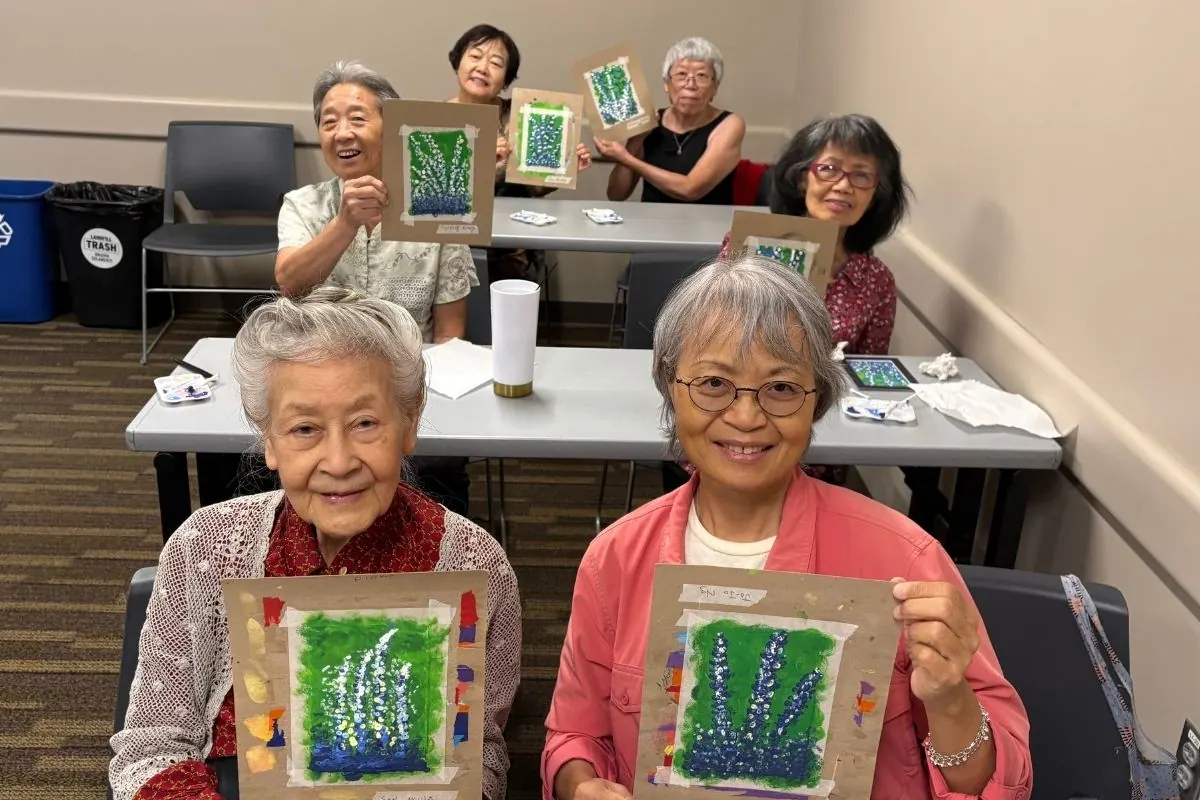 Six residents hold bluebonnet paintings mounted on cardboard, some seated and some standing.