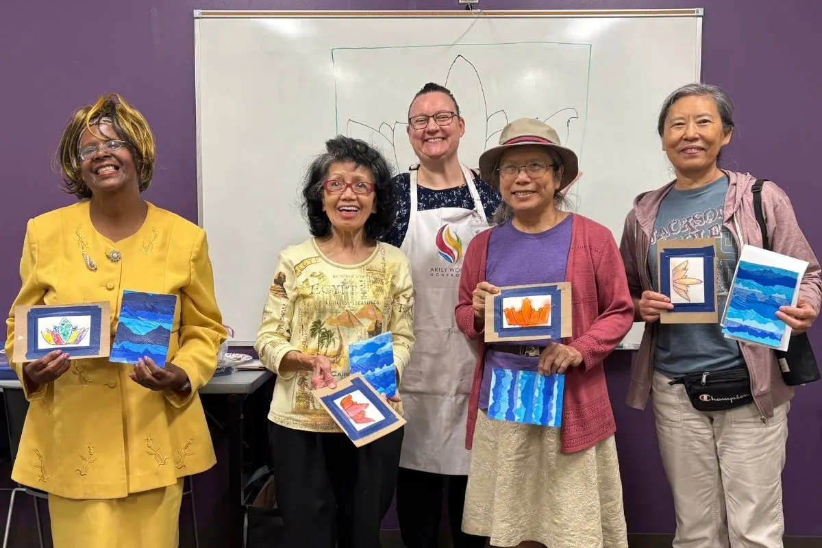 Four residents and a teaching artist hold framed watercolor artworks of mountains and colorful designs.