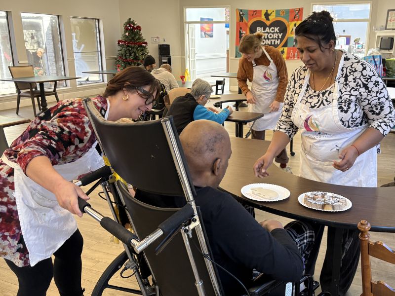 A participant using a wheelchair painting at an accessible-height easel, an artist kneeling beside them.