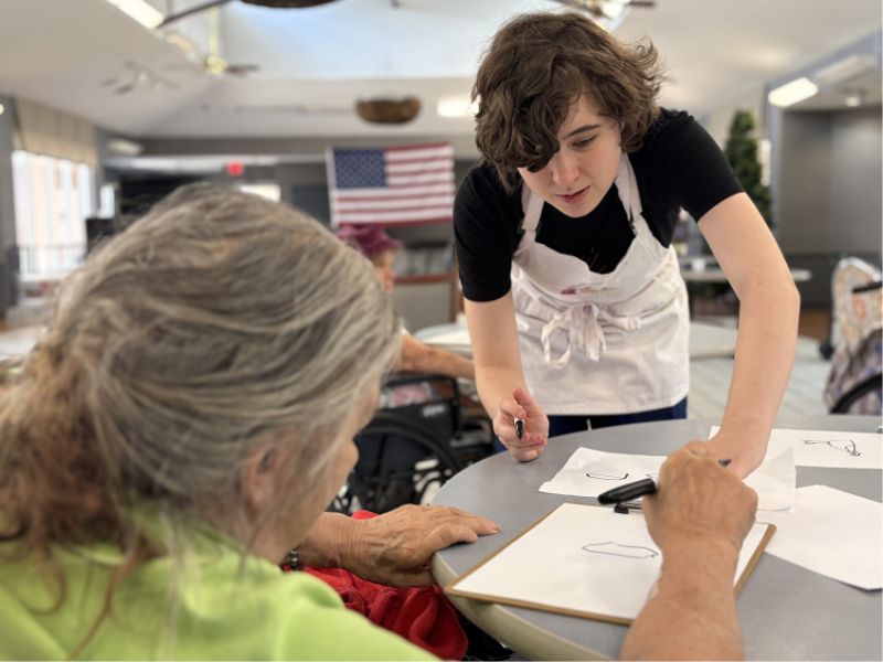 Two people signing to one another over a shared canvas, both smiling.