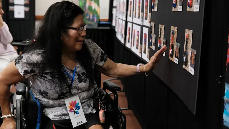 A senior artist reaches out to touch her painting on the wall.
