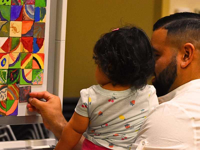 A happy family smiling with their finished artwork at a free Artly World family arts program in Austin, Texas